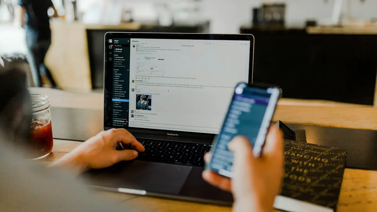 Pessoa revisando seu site em um notebook enquanto consulta o celular