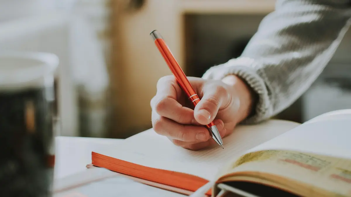 Mano escribiendo con bolígrafo naranja en un cuaderno abierto