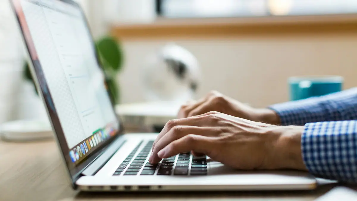 Manos escribiendo en el teclado de un portátil sobre un escritorio