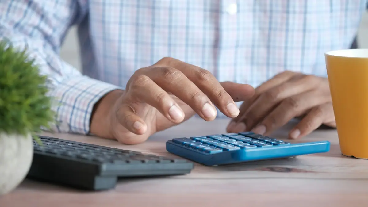 Persona usando una calculadora en el escritorio junto a un teclado