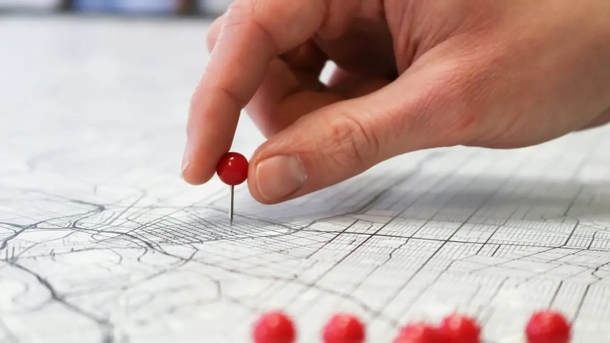 Mano clavando un alfiler rojo sobre un mapa de la ciudad
