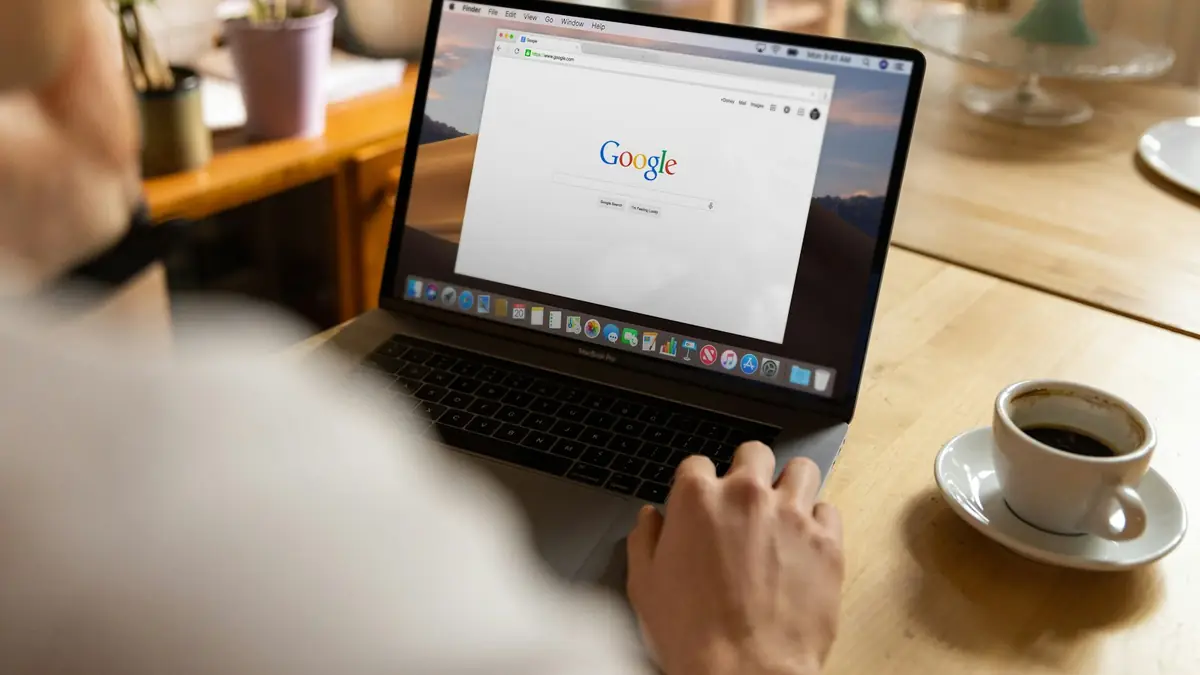 Person searching on Google from their laptop next to a cup of coffee