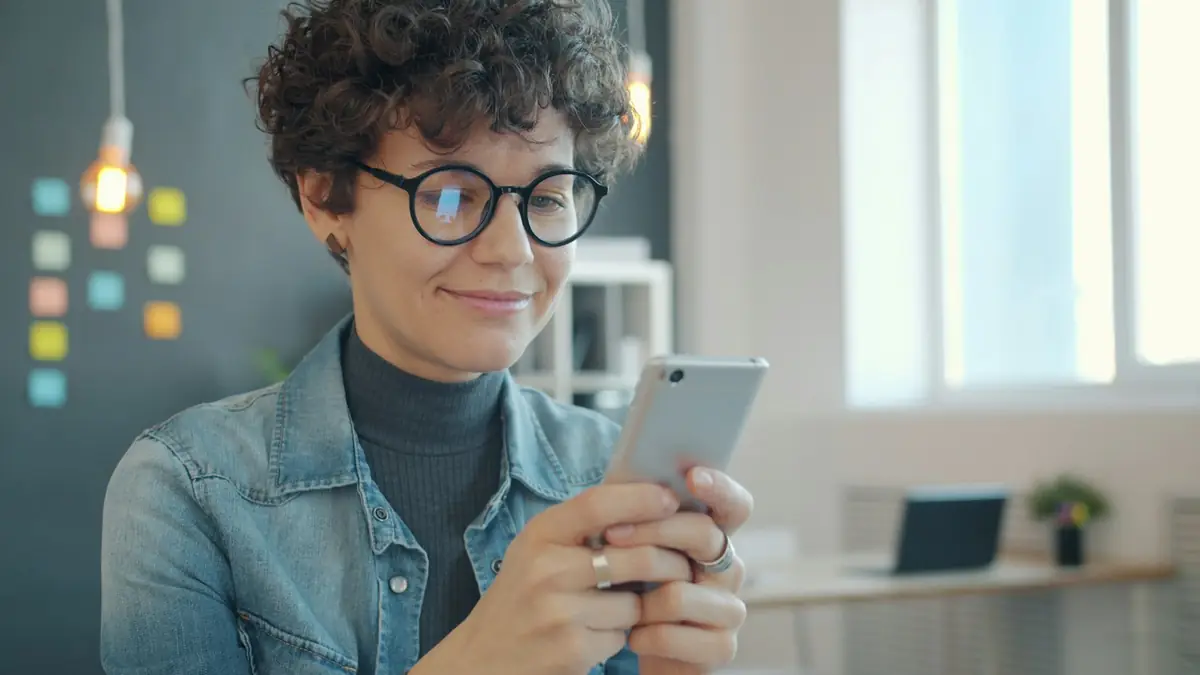 Mujer sonriendo mientras conversa por chat en su teléfono