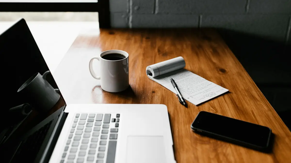 Escritorio de madera con portátil, taza de café, libreta y celular, listo para escribir el contenido de una web