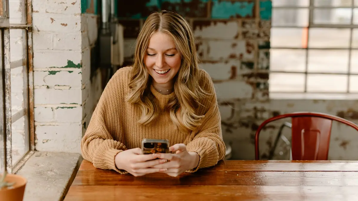 Mujer sentada en una mesa revisando su teléfono celular